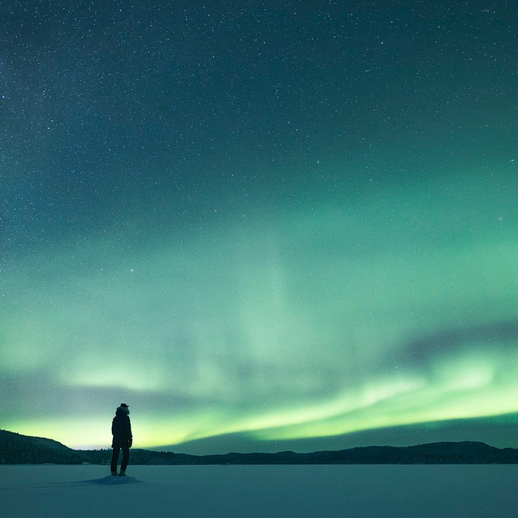 A person enjoying the northern lights on a frozen lake. | Lapland Luxury