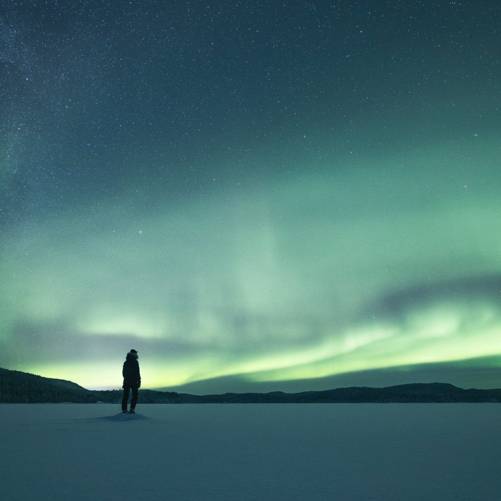 A person enjoying the northern lights on a frozen lake. | Lapland Luxury