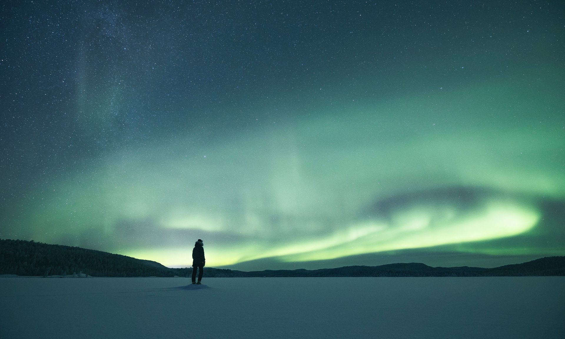 A person enjoying the northern lights on a frozen lake. | Lapland Luxury